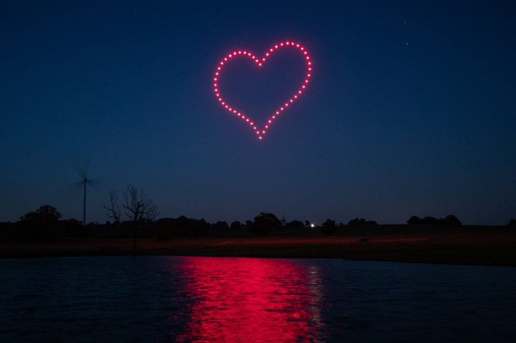 Cœur rouge formé par des drones se reflétant sur un lac